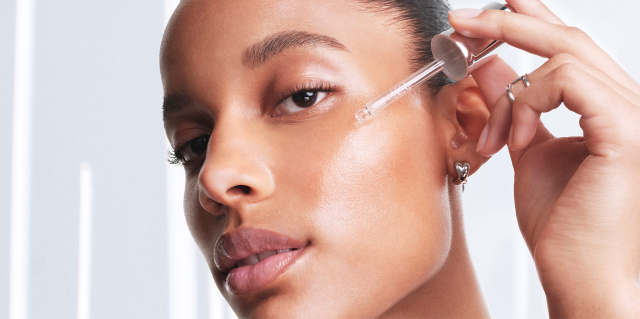 Woman with dark skin applying a hydrating hyaluronic acid serum to help with the skin moisture barrier and glow